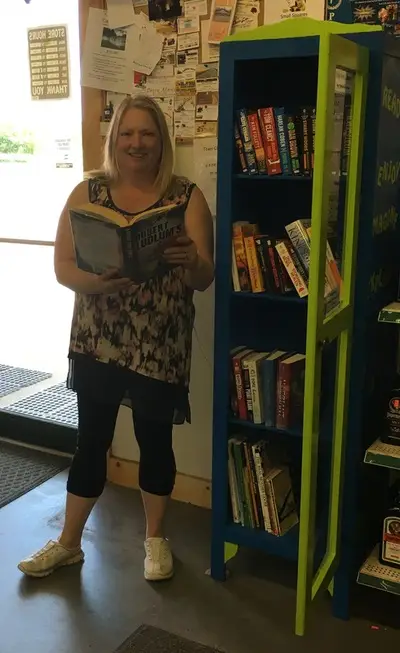 Betty holding a book next to a Little Free Library