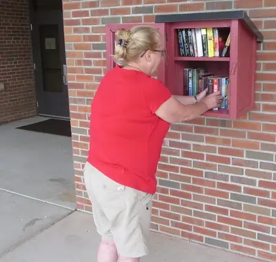 Woman stocking books into Little Free Library mounted outside on a brick wall outside