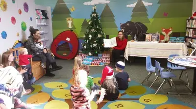 toddlers sitting on a rug in the library while being read to next to a Christmas tree