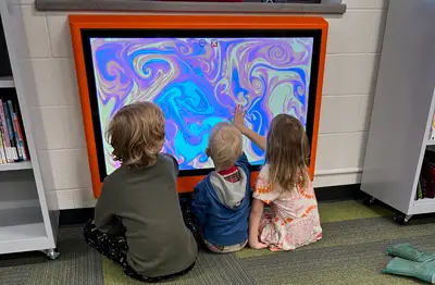3 toddlers interacting with the library's wall-mounted Touch2Play screen