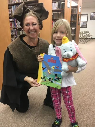 adult in costume and girl holding a the book "Jumbo" and a stuffed Jumbo toy
