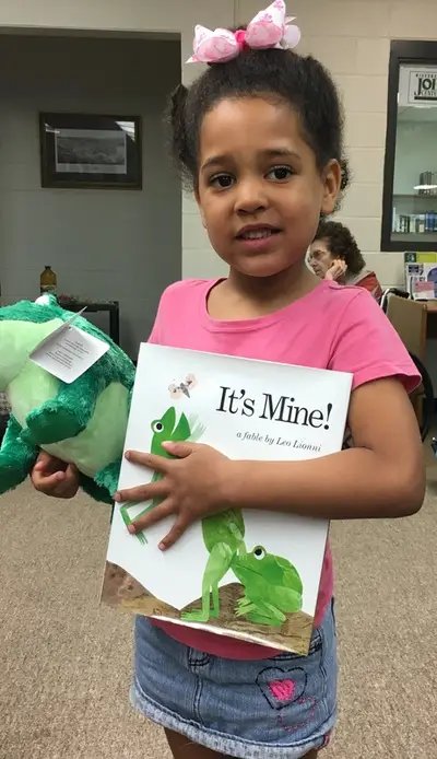 toddler holding stuffed frog toy and the book "It's Mine!"