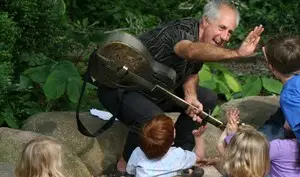 Stuart is holding a guitar and giving a high-five to a child as other children raise their hands